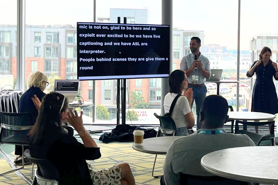 Audience watching a presentation with live CART captions on a large screen and an ASL interpreter