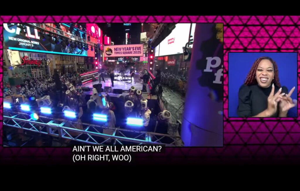 The 2025 livestream frame: the Times Square stage and marching band in the main window, the ASL interpreter in a panel on the right, and the caption 'Ain't we all American? (Oh right, woo)' below.