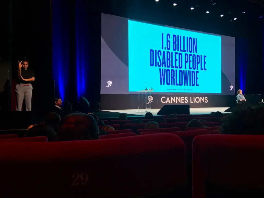 A presentation by Sinead Burke: she stands on stage right while an interpreter stands on stage left. A projected slide behind them reads, '1.6 billion disabled people worldwide.'