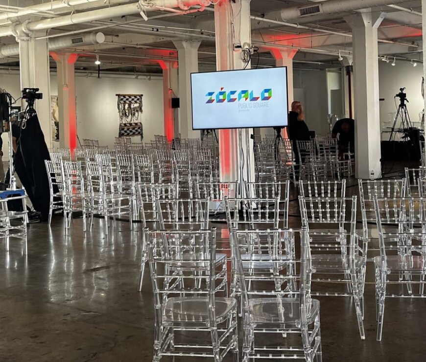 The Chicago room set before the audience arrives: rows of clear acrylic chairs facing a monitor showing the Zócalo Public Square logo, camera crews setting up at the sides of the gallery.