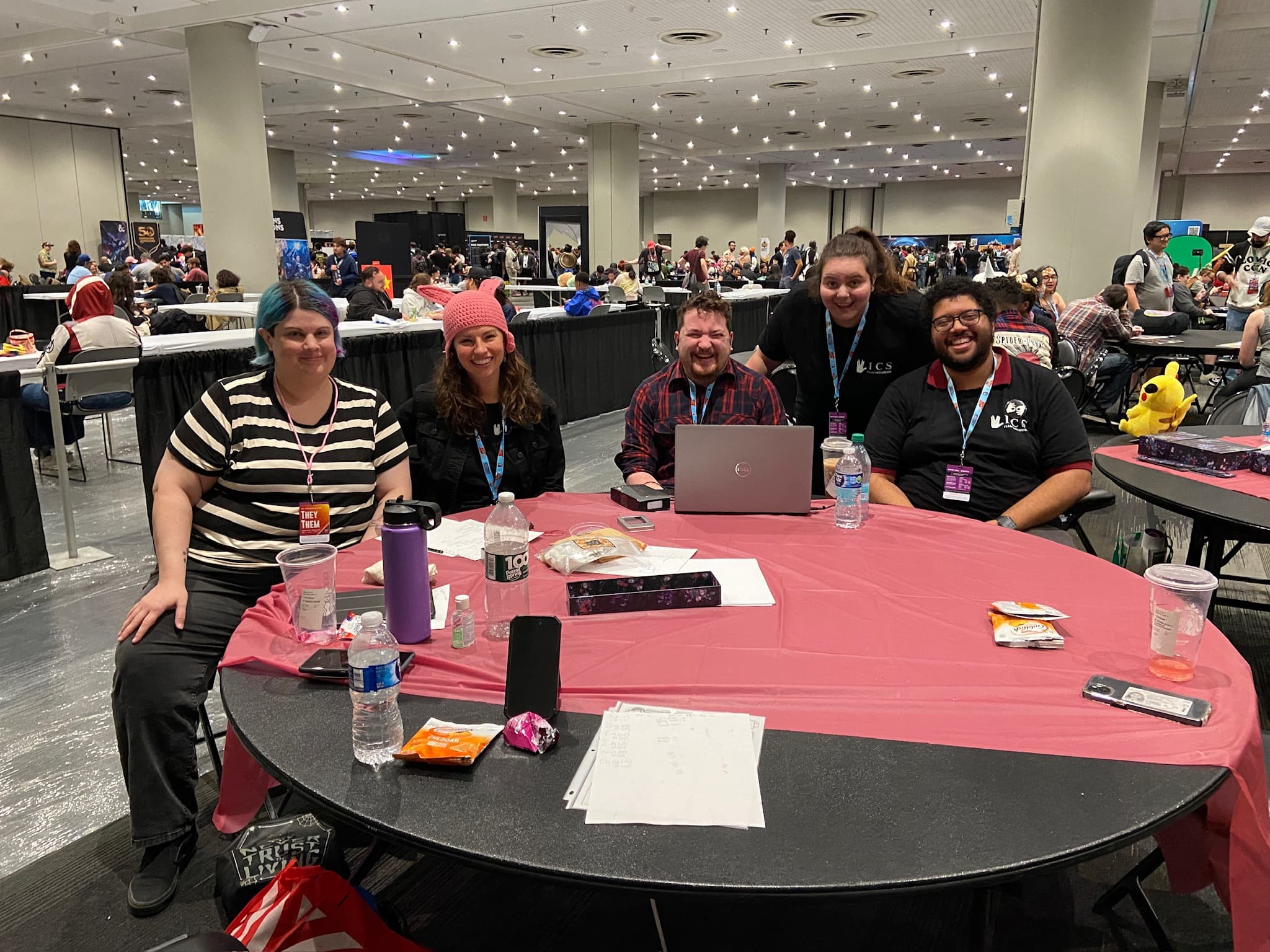 A group of five people are sitting around a circular table, smiling and enjoying themselves at Comic Con.