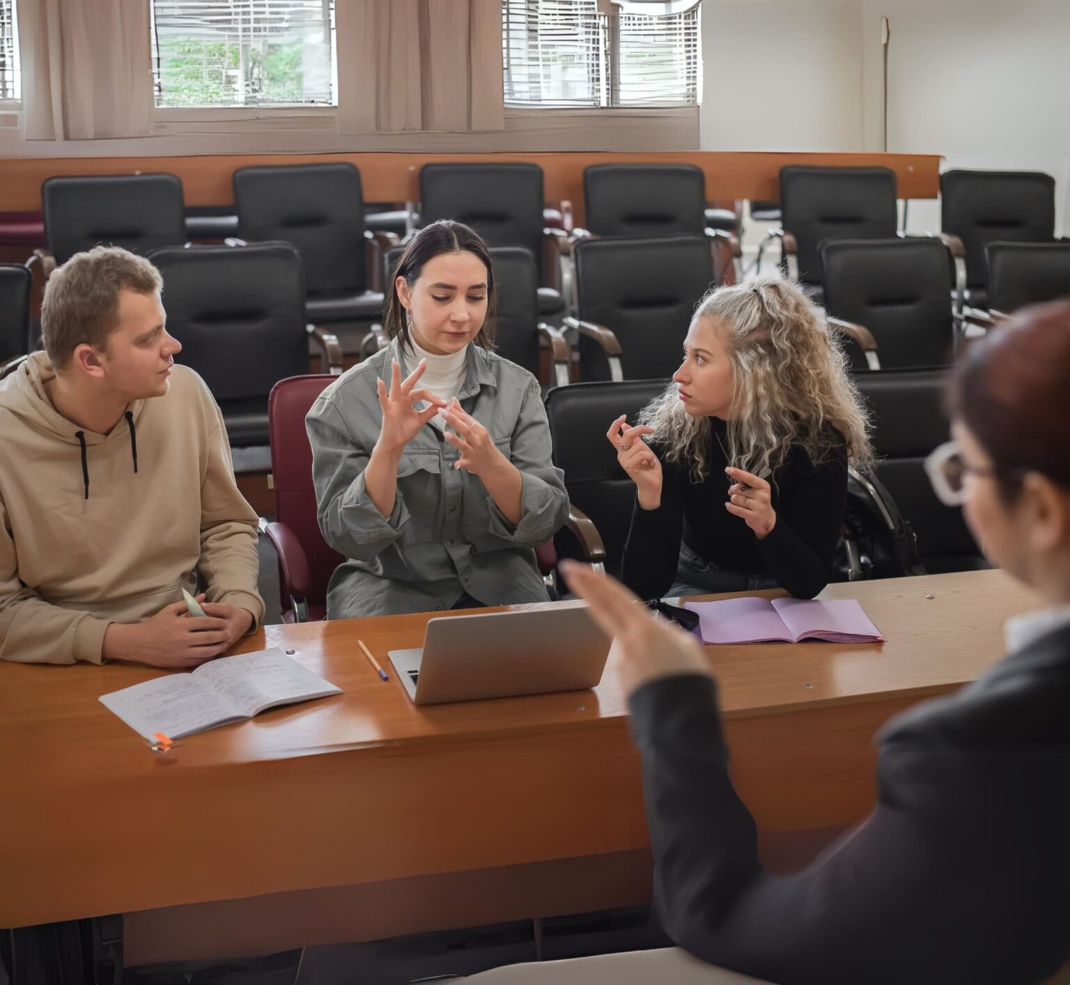 Three students signing to one another in a university lecture hall