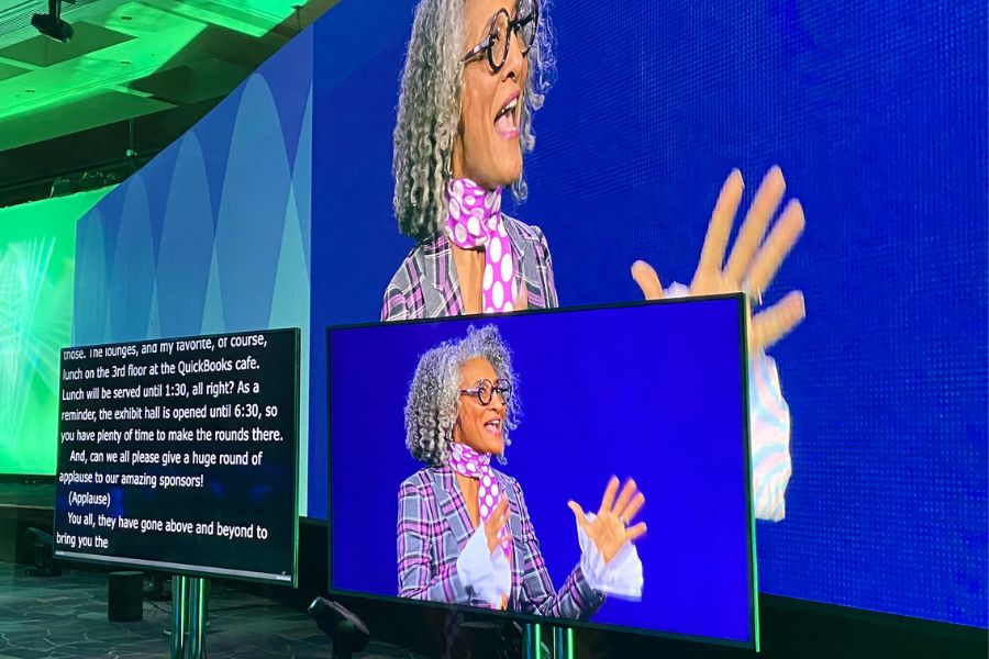 Speaker presenting on stage with live captions displayed on a large screen