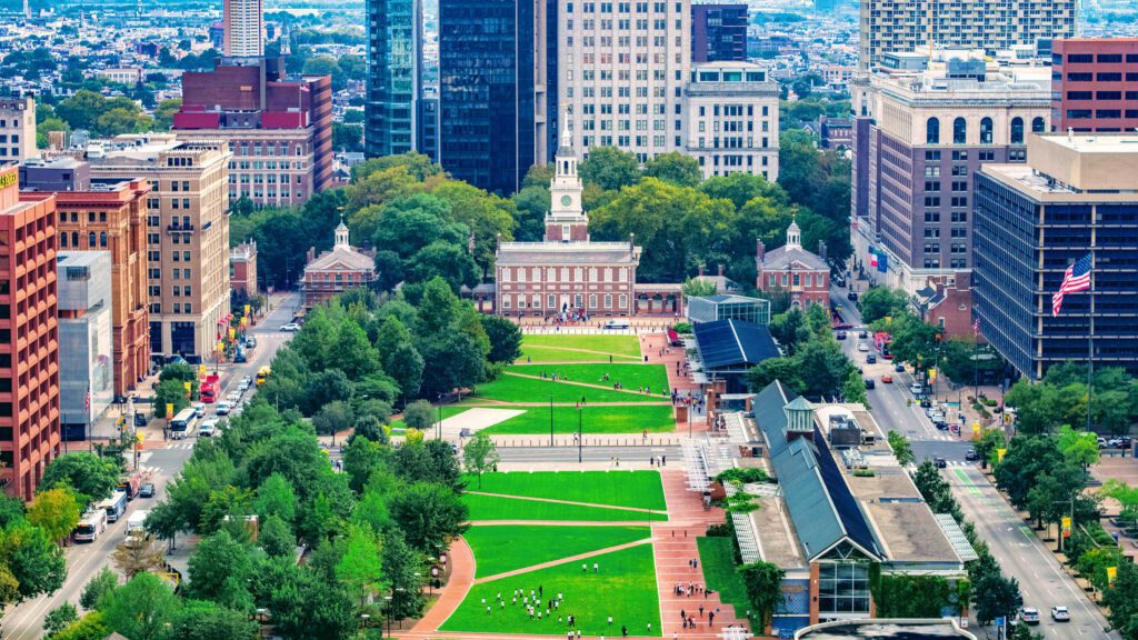 An aerial view of Independence Mall, with Independence Hall's white clock tower rising above the trees and green lawns between Center City's office towers.