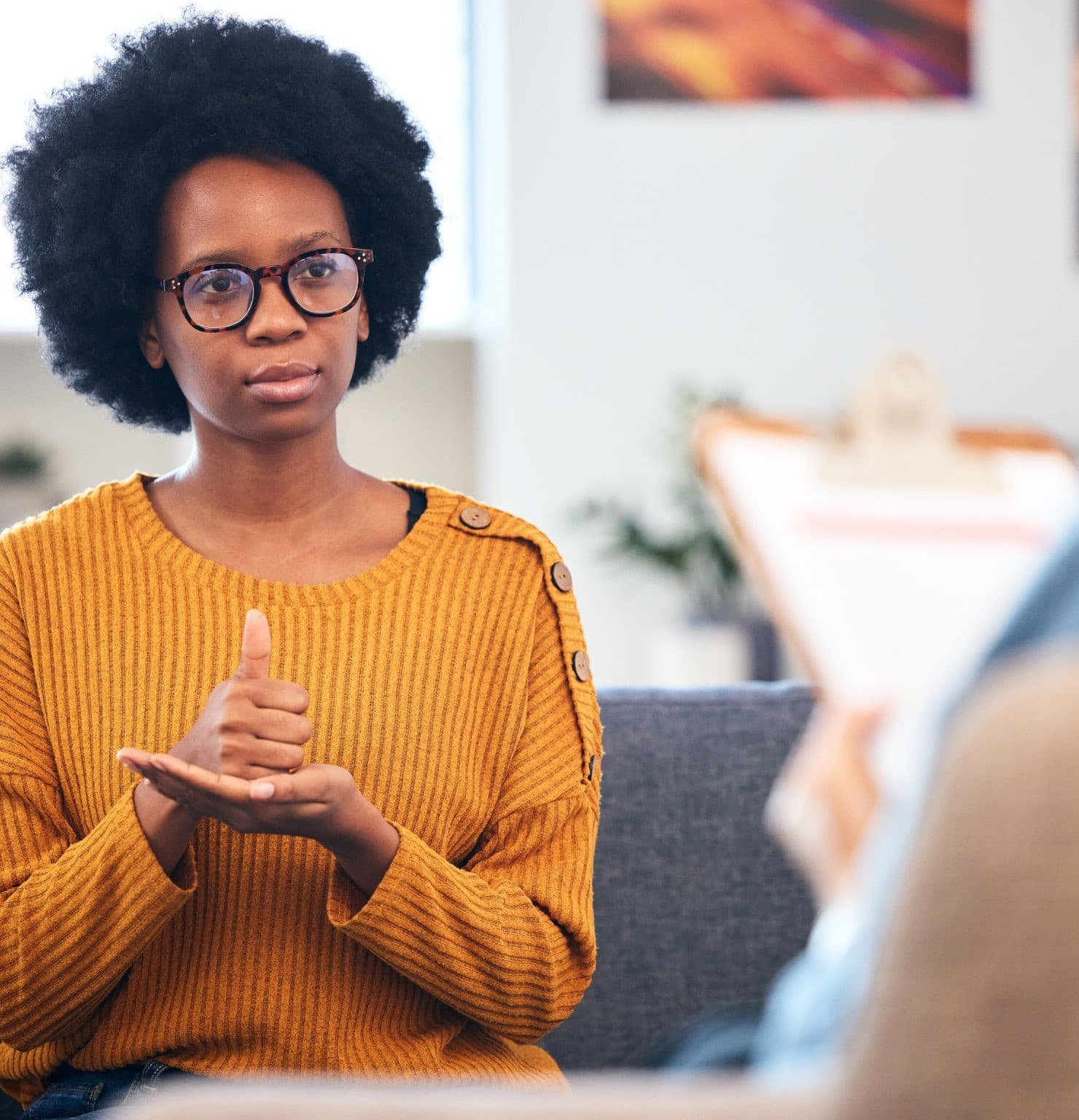 A woman in an orange sweater signing during a counselling session while a clinician takes notes