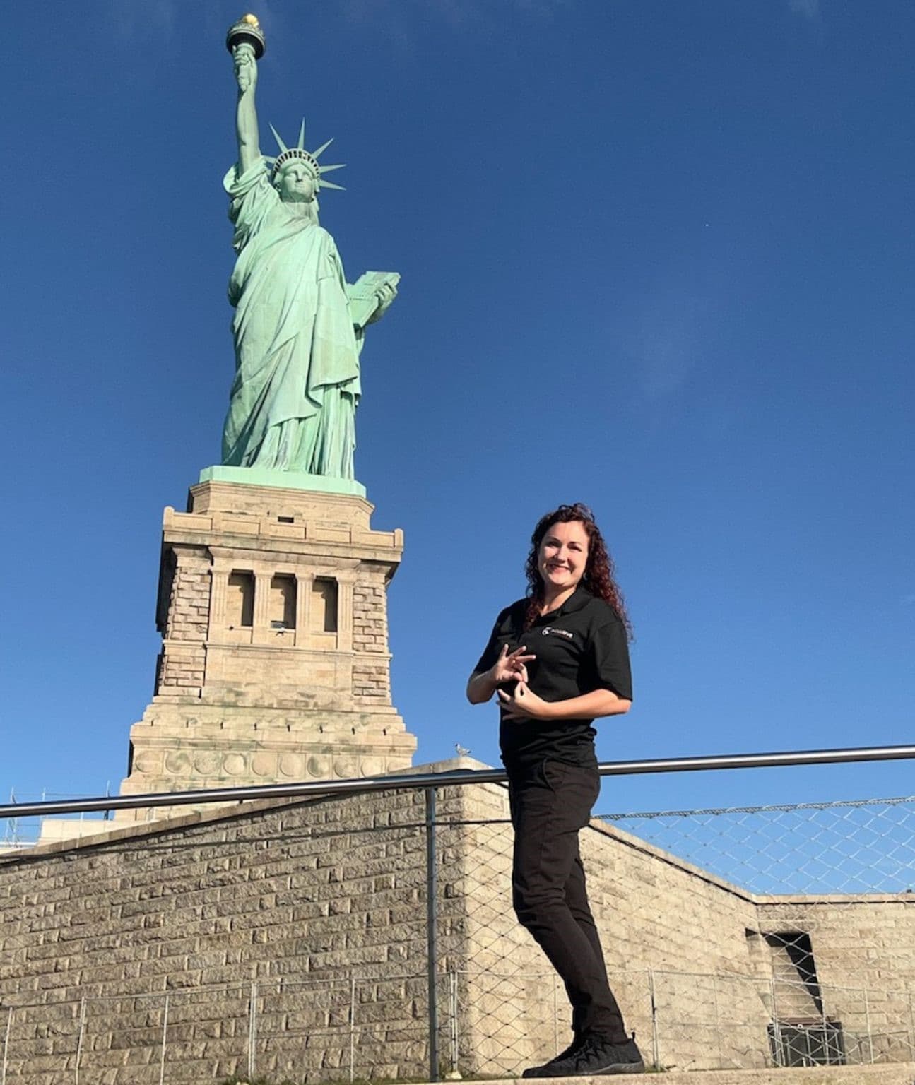 An interpreter signing on a walkway in front of the Statue of Liberty