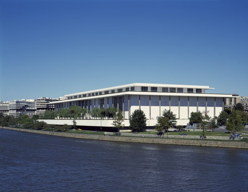 The John F. Kennedy Center for the Performing Arts lit at night above the Potomac, its colonnade reflected in the water.