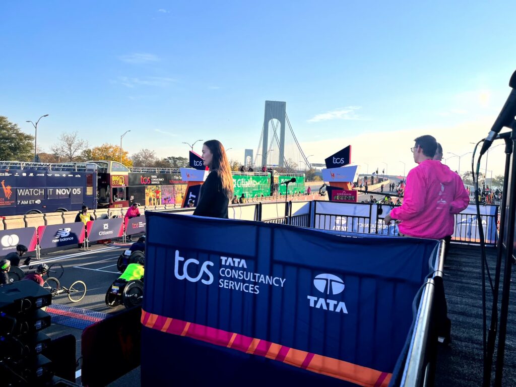 An ICS interpreter stands at the marathon start line on the Staten Island approach to the Verrazzano-Narrows Bridge, with handcyclists lined up behind the TCS barricade.