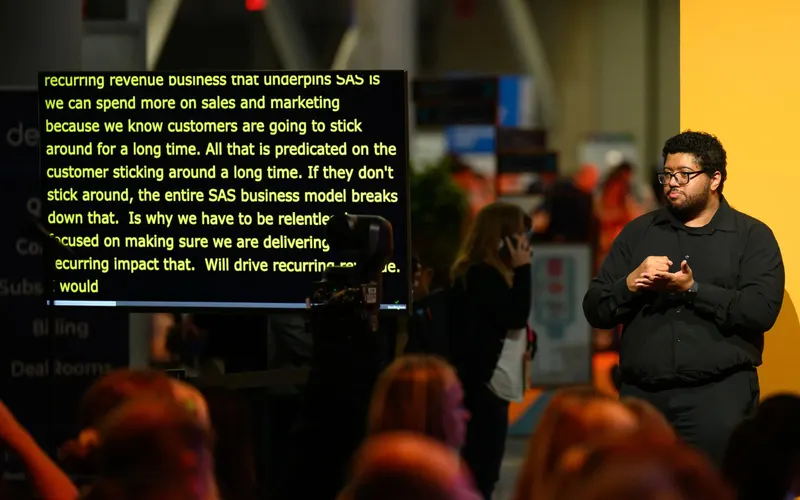 A speaker on stage beside a large screen showing live captions
