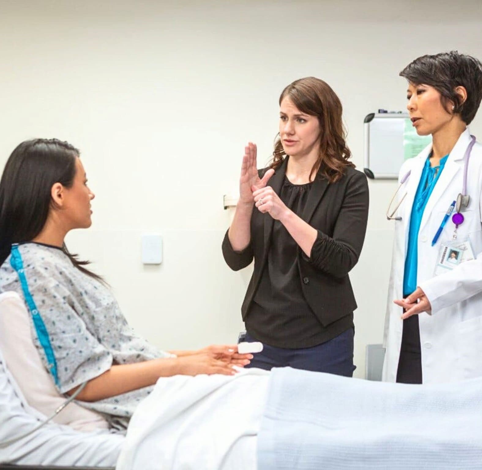 An interpreter signs between a hospital patient and her doctor in an exam room