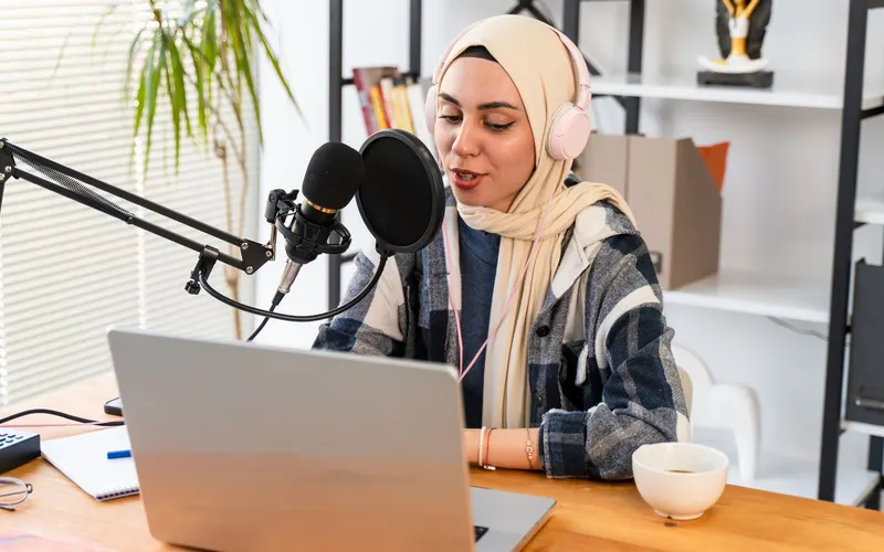 A voiceover artist recording at a microphone with headphones and a laptop