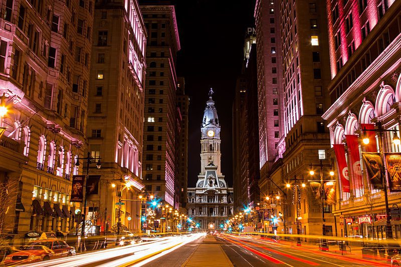 Philadelphia City Hall's illuminated clock tower at night, framed by the light trails of traffic down Broad Street.