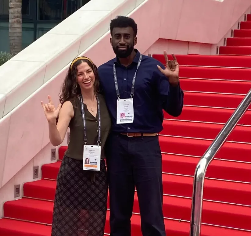 Frank, Cannes Lions Chief DEI Officer, and Rebecca, a Deaf attendee from 2024, pose together on the iconic red steps, both holding up the ILY sign.