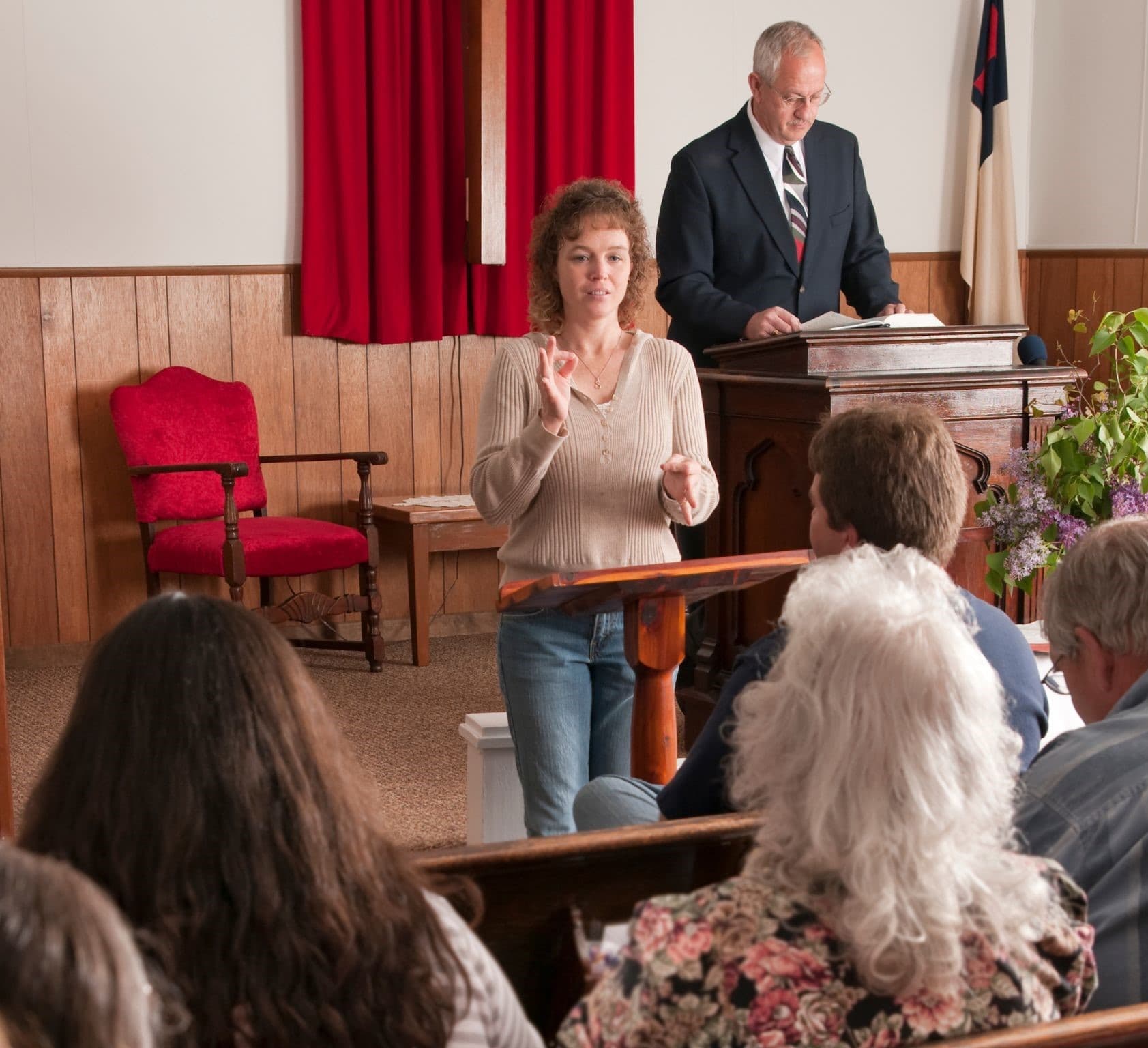 An interpreter signs to a congregation while a pastor reads from the pulpit