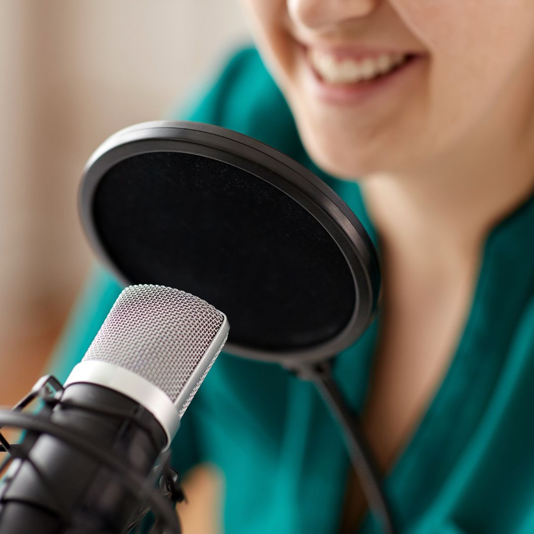 A studio microphone with a pop filter, with a smiling person in the background.