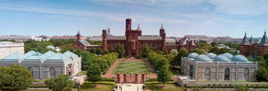 The red sandstone towers of the Smithsonian Castle behind the clipped parterre of the Haupt Garden, with a low domed pavilion at each side of the walk.