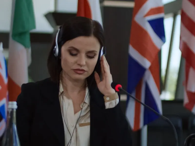 An interpreter listening through headphones at a conference table lined with national flags