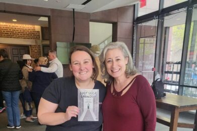 Two people stand together in the church lobby after a performance, one holding up a “Lost Sock Laundry” programme to the camera.