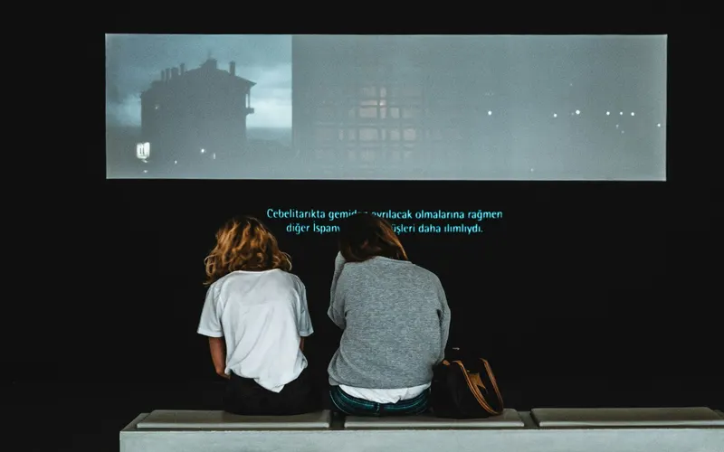 Two people watching a film with multilingual subtitles on screen