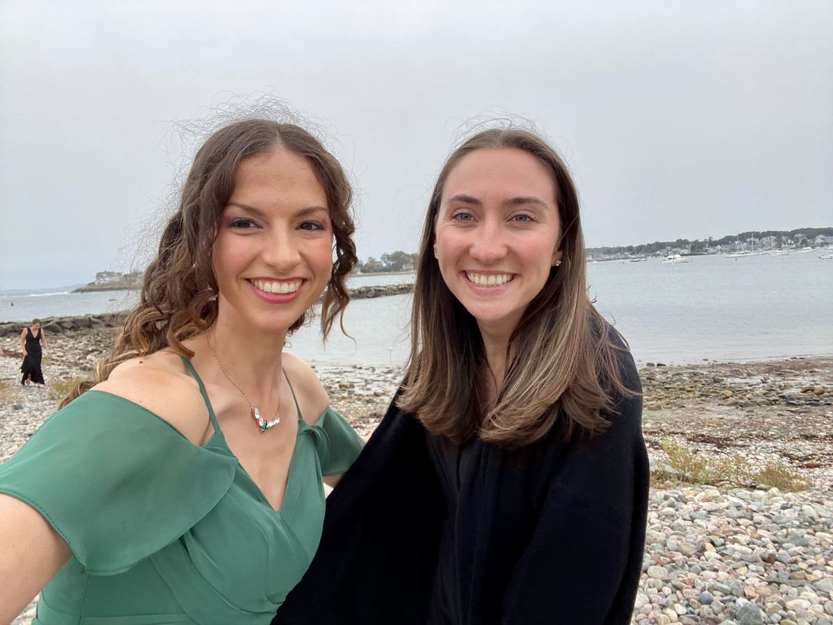 A calming beach background. Rebecca, in a green dress, and a female ASL interpreter in a black sweater are posing and smiling for a selfie.