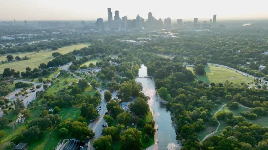 The lawns of Zilker Park with the downtown Austin skyline rising beyond the treeline.